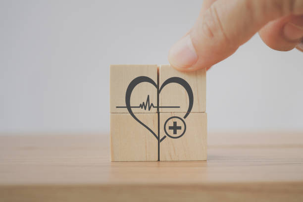 senior's hand arrange heart shape with clinic or hospital sign on wooden cube block with copy space for health check up, awareness of wellness, wellbeing, world health day concept - 语音交护 個照片及圖片檔